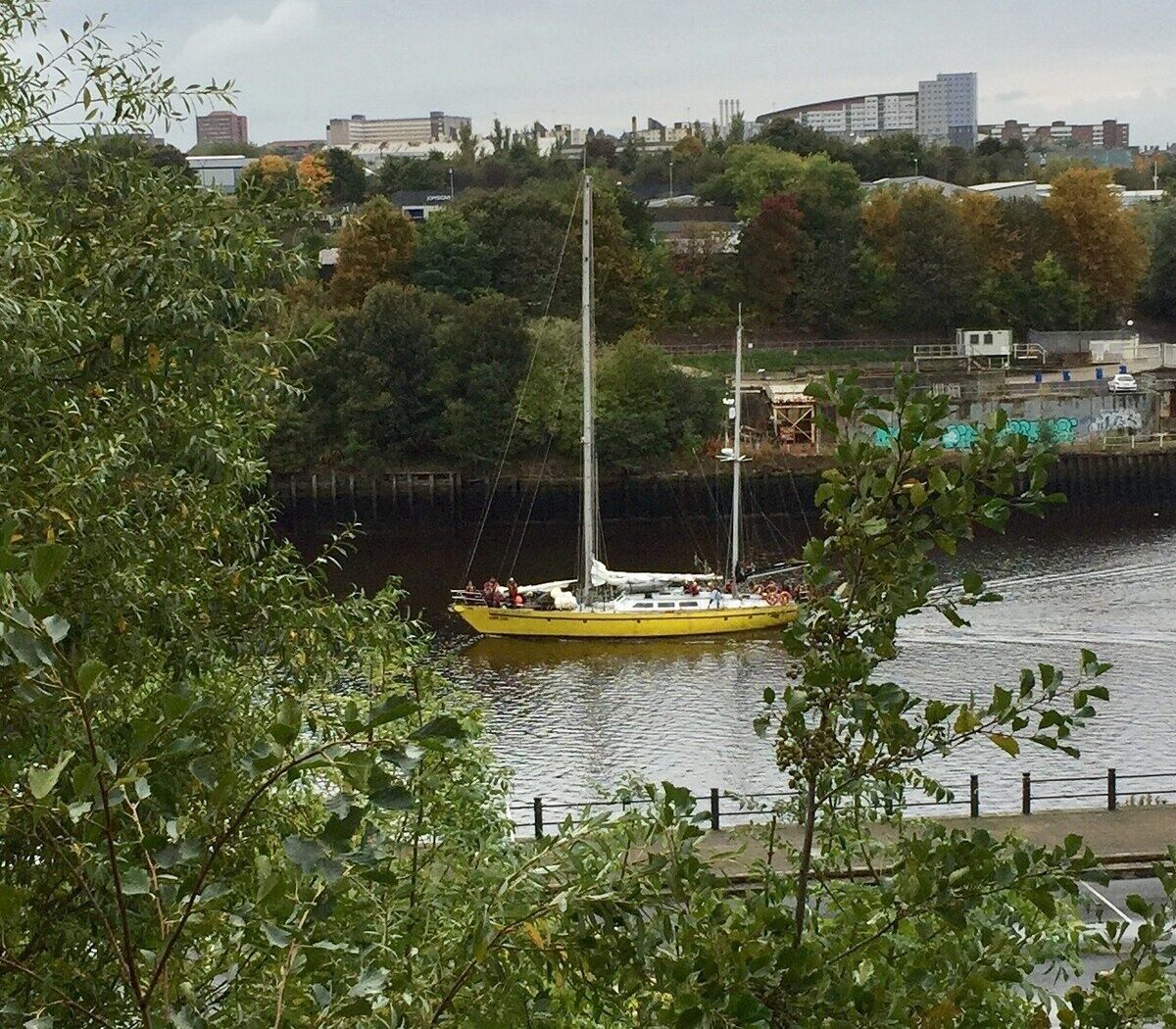 Um barco amarelo em um rio, com um horizonte urbano ao fundo.