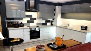 A modern kitchen with white cabinets, a black stove, and a dining area with a red leather couch and a small table. - Luxury Ouseburn flat with city & river views (Tyne and Wear)