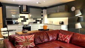 A modern living room with a leather sofa, a dining table, and a kitchen in the background. - Luxury Ouseburn flat with city & river views (Tyne and Wear)
