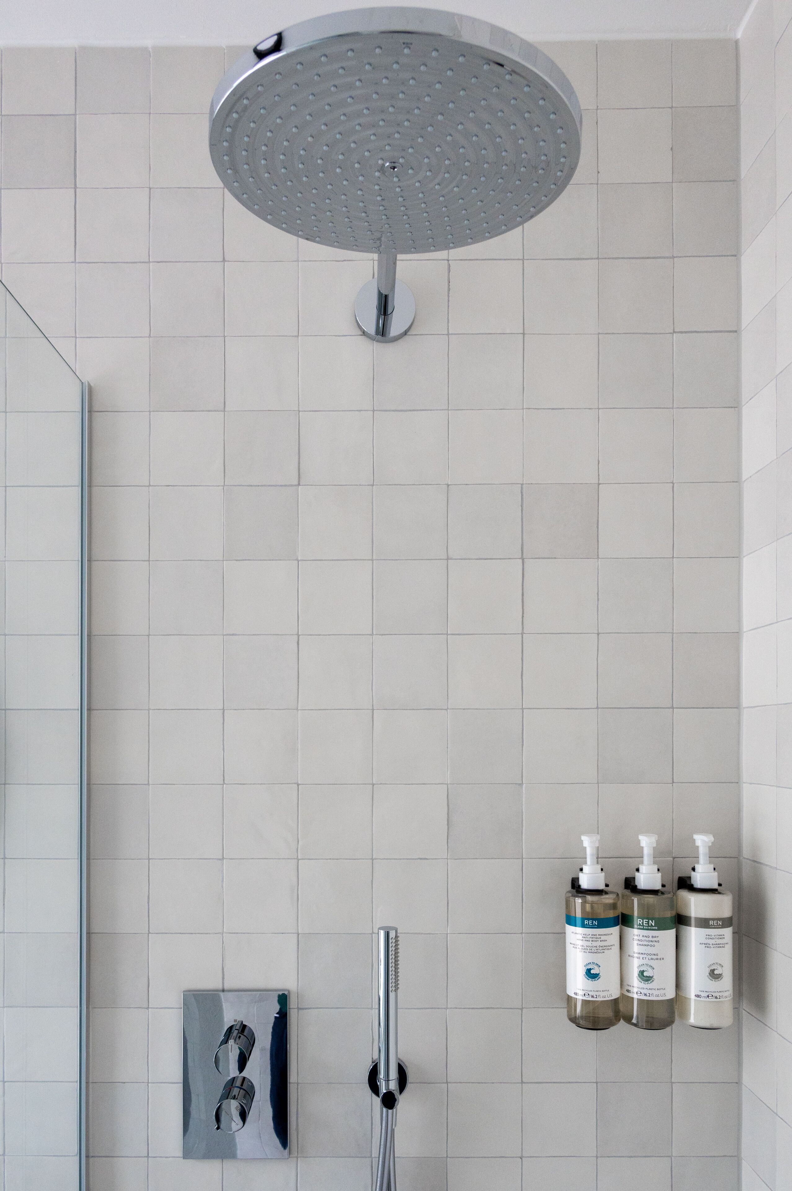 Ein modernes Badezimmer mit Duschkopf, einer Duschkabine aus Glas und drei Kosmetikflaschen an der Wand.
