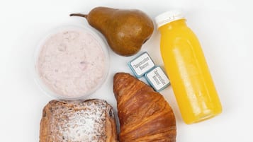 A breakfast setting with a pear, a croissant, a slice of bread, a container of yogurt, two packets of butter, and a bottle of orange juice.