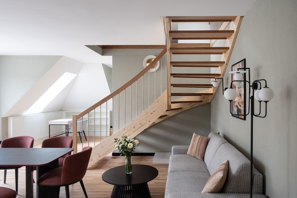 Un intérieur moderne avec un escalier en bois, une table ronde entourée de chaises, un canapé et un lampadaire.