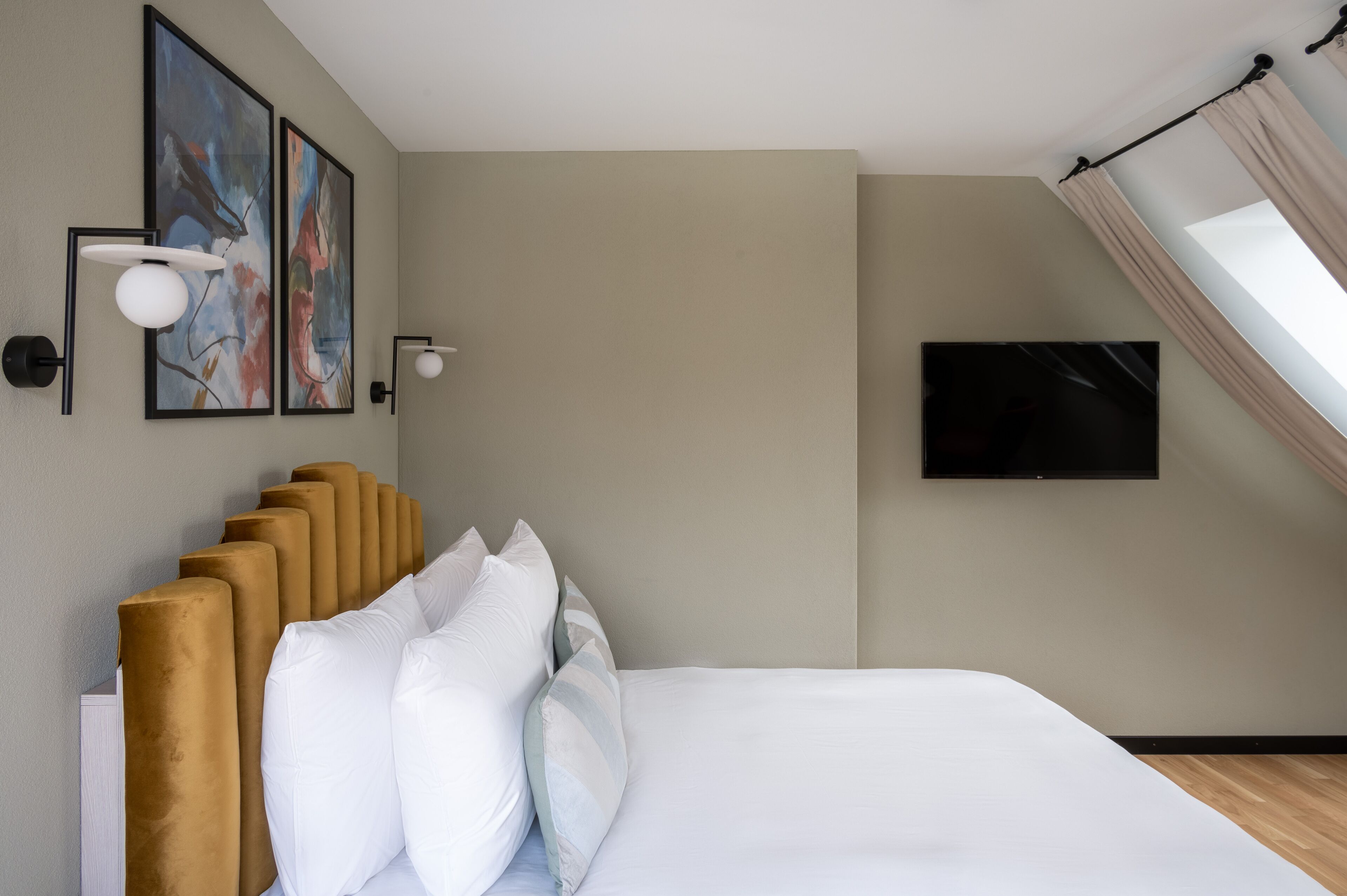 Una habitación de hotel moderna con una cama grande, un televisor de pantalla plana en la pared y dos cuadros abstractos.