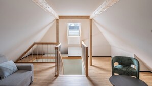 A loft bedroom with a wooden staircase, a small window, and a chair. - Numa Zurich Craft (Zürich)