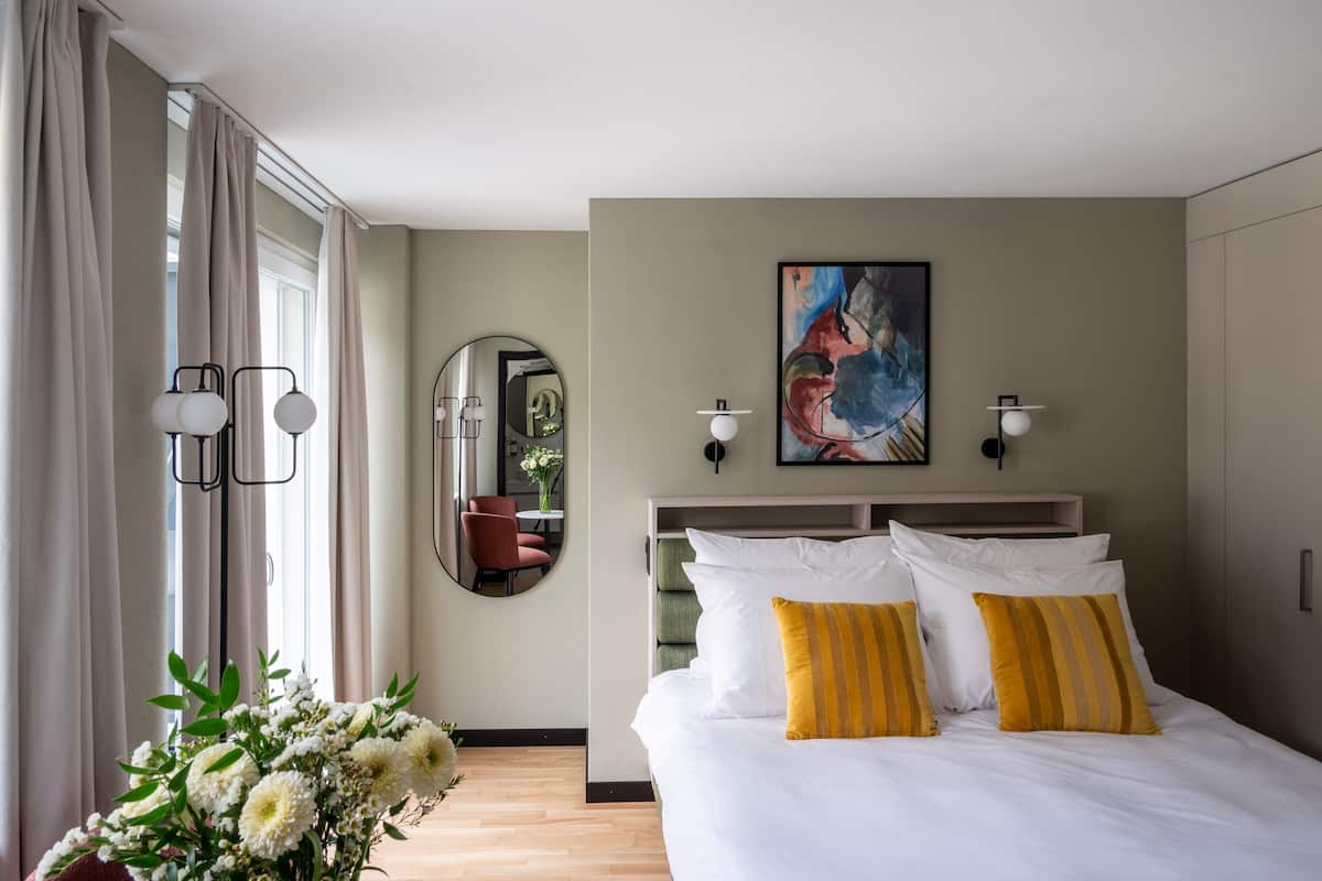 Une chambre d’hôtel avec un lit, un miroir, un tableau et un vase de fleurs.