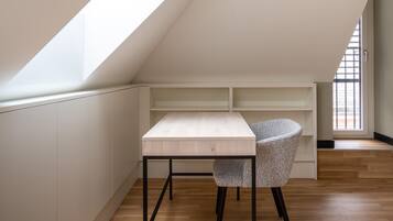 Una habitación pequeña y moderna con techo inclinado, un escritorio de madera con silla y estanterías integradas.