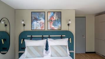 Un dormitorio moderno con un cabecero verde azulado, dos cuadros abstractos, lámparas de noche y un armario.