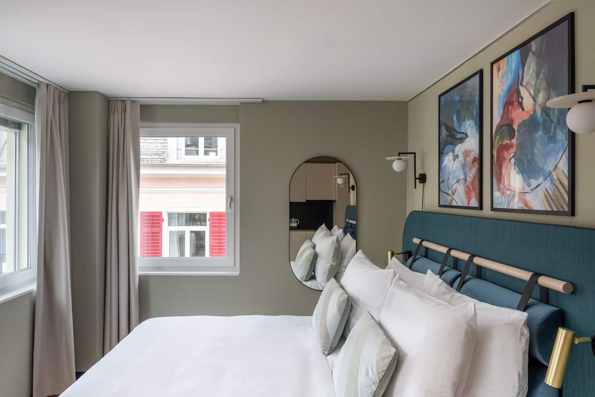 Une chambre d’hôtel avec un grand lit, un miroir rond et deux tableaux abstraits accrochés au mur.