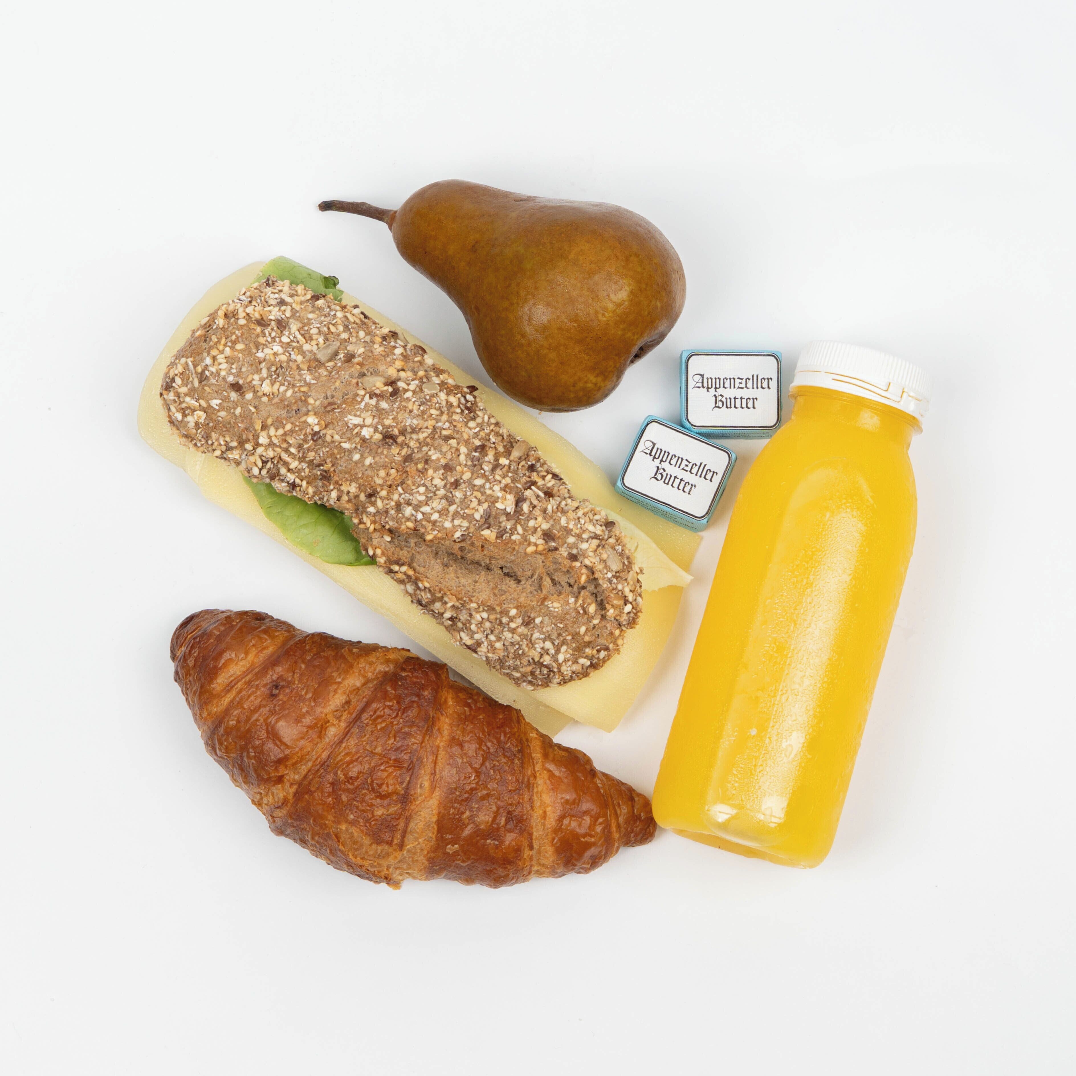 Una pera, una rebanada de pan con semillas, un croissant y una botella de jugo.
