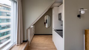 A modern hotel room with a wooden floor, a large window with curtains, a mirror, and a wall-mounted light fixture. - Numa Zurich Craft (Zürich)