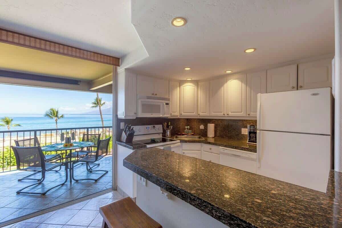 A kitchen with a view of the ocean, a dining area with outdoor seating, and a balcony with a railing.