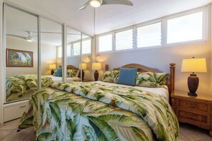 Un dormitorio con una cama grande, un ventilador de techo, una mesita de noche con lámpara y un espejo amplio.
