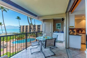 A balcony with a pool view, a dining area with chairs, and a kitchen area.