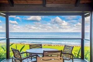 A balcony with a table and chairs, overlooking a beach and ocean.