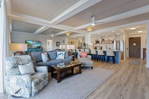 A spacious living area with a sofa, armchair, and coffee table, a kitchen with a refrigerator and bar stools, and a dining area with a table and chairs.