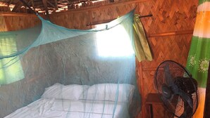 A room with a bed covered by a mosquito net, a fan, and a wooden wall.