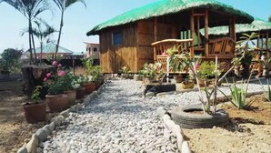 A rustic wooden house with a thatched roof, surrounded by potted plants and a gravel pathway.