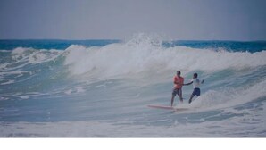 Zwei Personen surfen auf einer Welle im Meer.