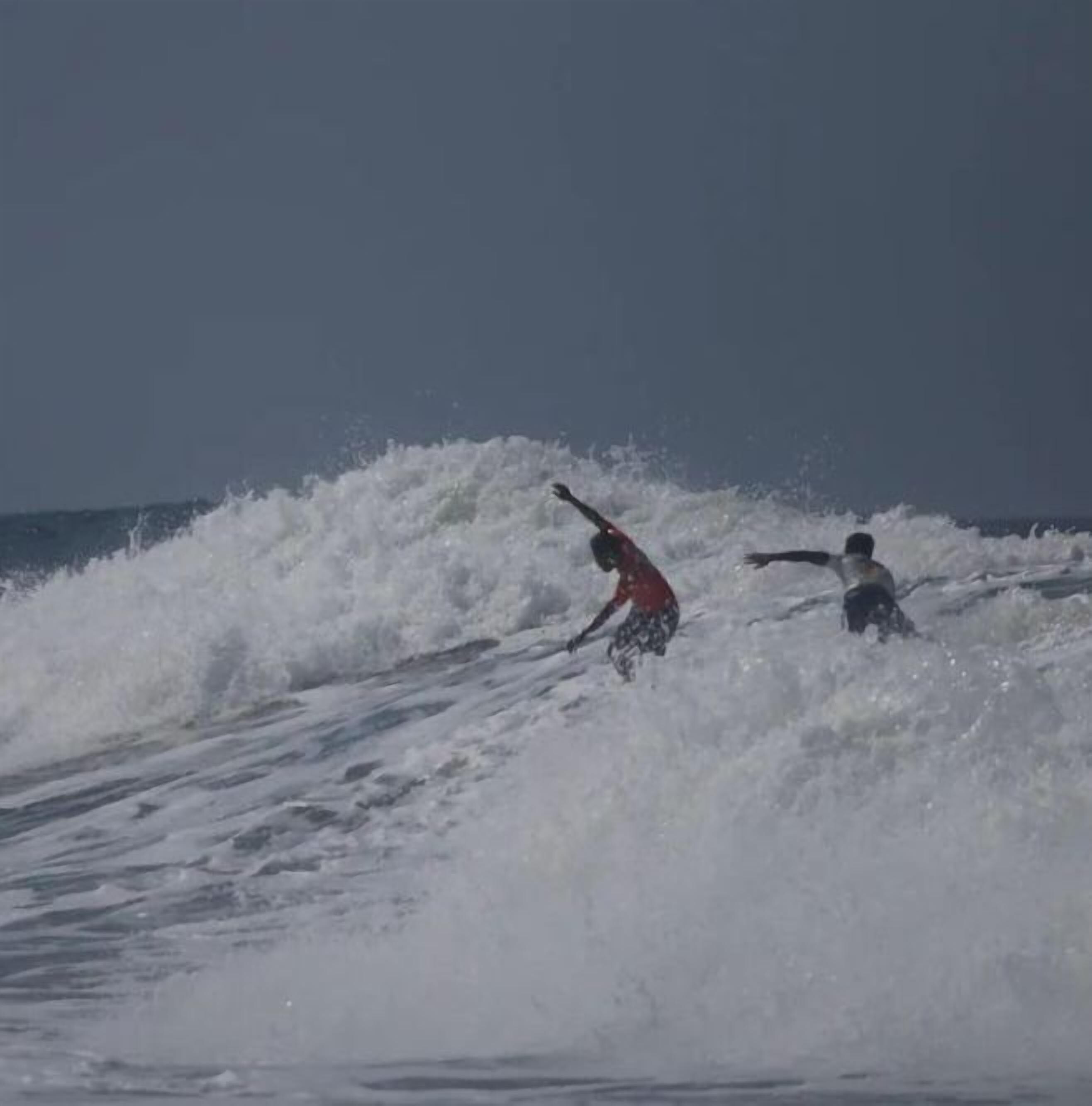Twee surfers rijden over een golf.