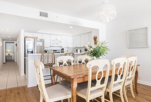 Cozinha moderna com armários brancos, mesa de jantar de madeira e lustre.