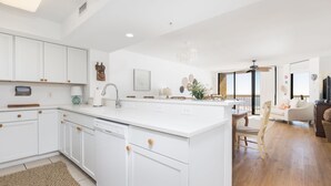 A spacious kitchen with white cabinetry, a central island, and a dining area with a wooden table and chairs. - Stay @ Folly Ha'i on Folly Beach (Folly Beach)