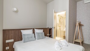 A hotel room with a wooden headboard, a bed with white linens, a set of towels, and a wooden ladder leaning against the wall. - Florella Residences 3 pièces Marceau (Cannes)