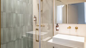 A modern bathroom with a glass shower enclosure, a white sink, and a mirror above it. - Florella Residences 3 pièces Marceau (Cannes)
