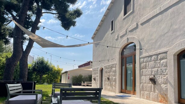 An outdoor seating area with metal chairs and a table, a string of lights, and a building with stone walls and a wooden door. - BB Delle Murge (Corato)