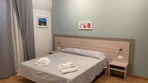 A neatly made bed with a grey quilt, two bedside tables, a wall-mounted picture, and a grey curtain. - BB Delle Murge (Corato)