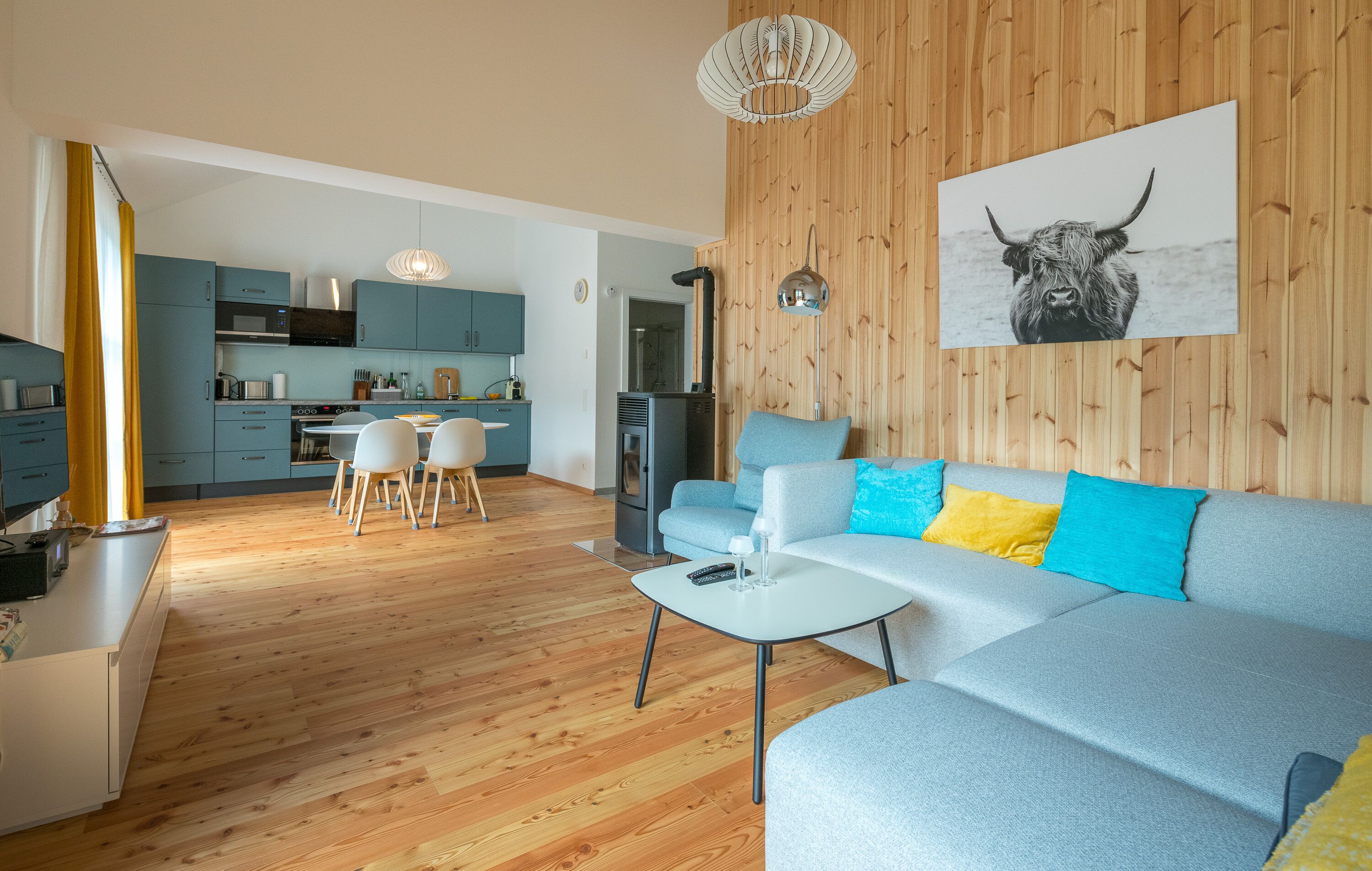 A modern living room with a grey sofa, a small white table, and a kitchen in the background.