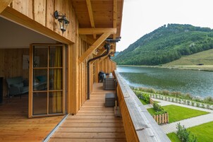 Um deck de madeira com uma porta de vidro que dá para um quarto, com vista para um lago e colinas.