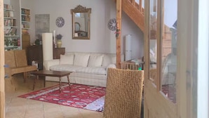 Una sala de estar con un sofá, una silla de mimbre, un tapete rojo estampado, techo de madera y una escalera.