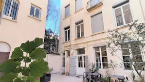 Un patio con un edificio, una reja y mobiliario exterior.