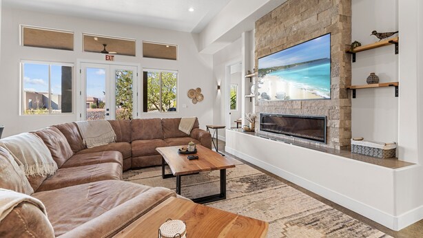 Una sala de estar moderna con un sofá seccional, chimenea, televisor grande y una pared de acento de piedra.