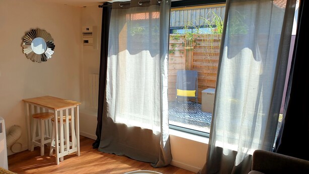 Een kamer met een houten tafel, een klein krukje, een spiegel en een raam met gordijnen.