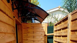 Een houten terras buiten met een metalen rooster vloer, omgeven door houten wanden en een overdekt gedeelte.