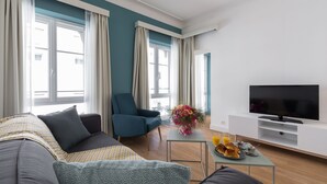 Een moderne woonkamer met een bank, fauteuil, flatscreen-tv, een klein tafeltje met ontbijt en grote ramen.