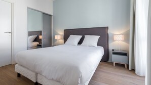 Een moderne slaapkamer met een groot bed, nachtkastjes met lampen, en een kledingkast.
