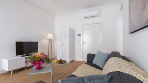 Een moderne woonkamer met een bank, een televisie, een kleine tafel met een bloemenvaas en een lamp.
