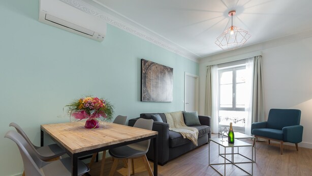 Een moderne woonkamer met een eettafel, twee banken, een salontafel en een groot raam met gordijnen.