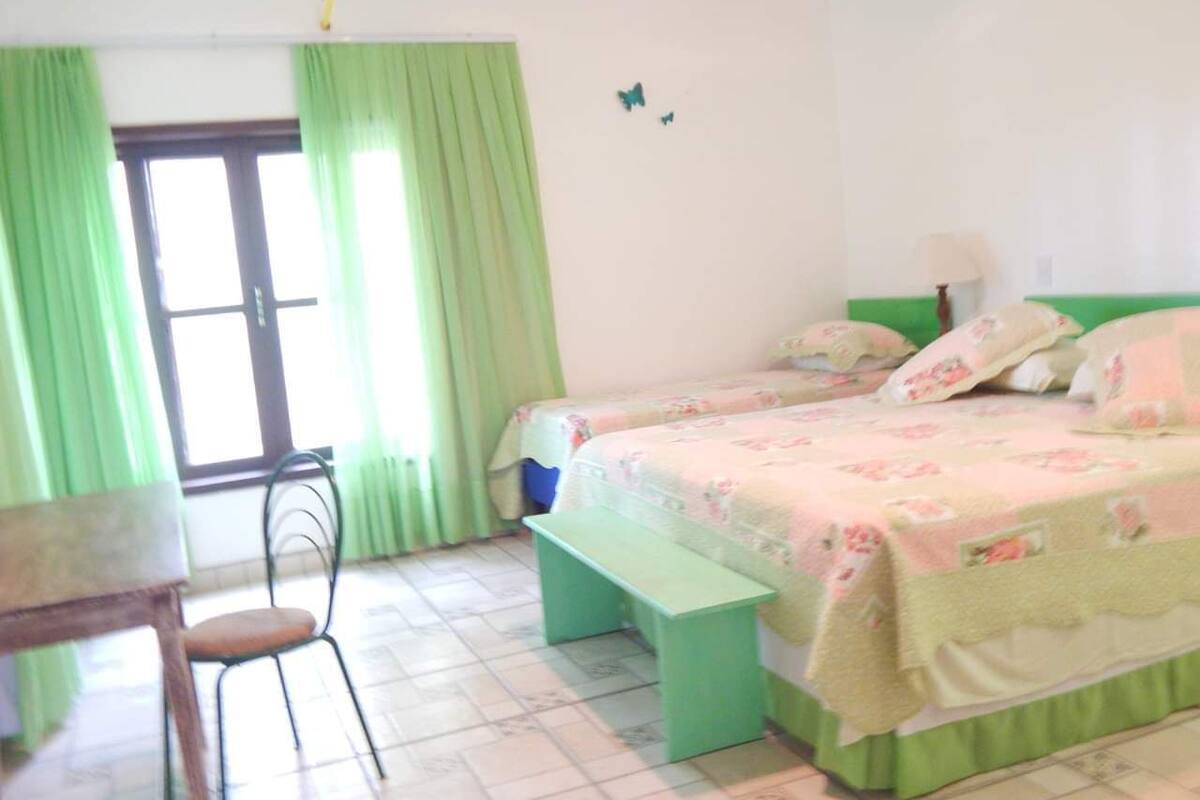 Une pièce comprenant un lit, un bureau, une chaise et une fenêtre avec des rideaux.
