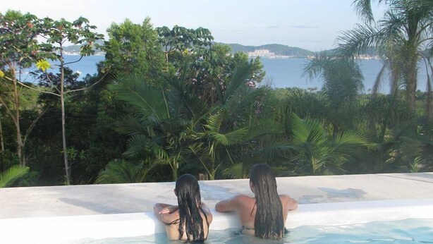 Dues persones relaxant-se en una piscina amb vista al mar i vegetació exuberant.