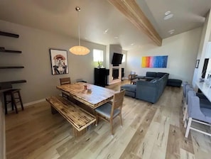 A spacious living area with a wooden dining table, a blue sofa, and a TV mounted on the wall.