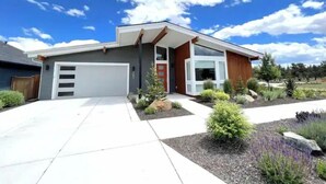 Ein modernes, zweistöckiges Haus mit Garage, überdachter Veranda und einem angelegten Vorgarten mit verschiedenen Pflanzen und einem kleinen Baum.