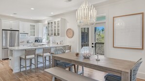 Una cocina moderna con armarios blancos, una isla de madera con taburetes altos y una araña.