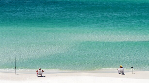 Dos personas pescan en una playa con agua turquesa cristalina.