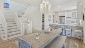 Una cocina moderna con armarios blancos, un refrigerador de acero inoxidable y un comedor con mesa y sillas de madera.