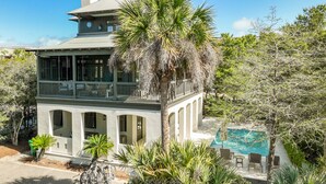 Una casa de dos pisos con balcón, piscina y follaje circundante.