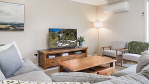 A living room with a wooden coffee table, a sofa, a TV on a wooden stand, a lamp, and a chair.