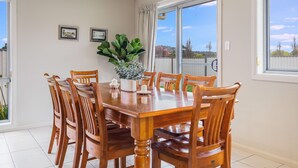 A dining area with a wooden table and chairs, a potted plant, and framed pictures on the wall.